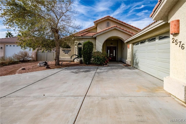 mediterranean / spanish-style house featuring a garage, driveway, a tiled roof, and stucco siding