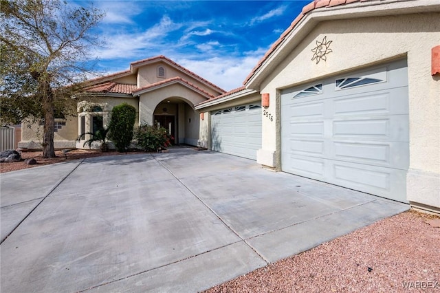 view of front of home featuring a garage, a tile roof, concrete driveway, and stucco siding