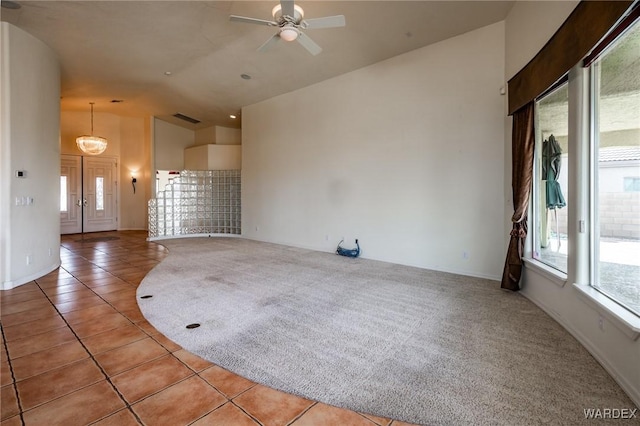 unfurnished living room with ceiling fan with notable chandelier, light carpet, visible vents, and light tile patterned flooring