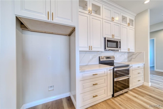 kitchen featuring white cabinets, glass insert cabinets, stainless steel appliances, light wood-style floors, and backsplash