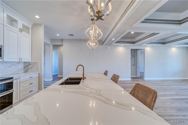 kitchen with white cabinets, glass insert cabinets, light stone counters, stove, and a sink