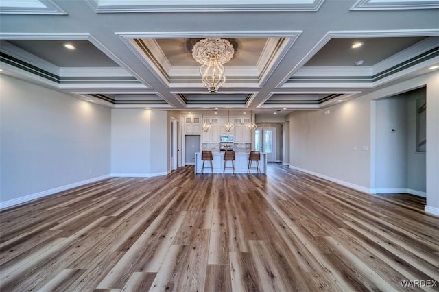 unfurnished living room featuring crown molding, baseboards, wood finished floors, and a notable chandelier