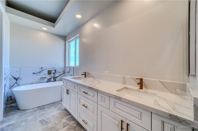 full bath featuring a freestanding bath, double vanity, a sink, and recessed lighting