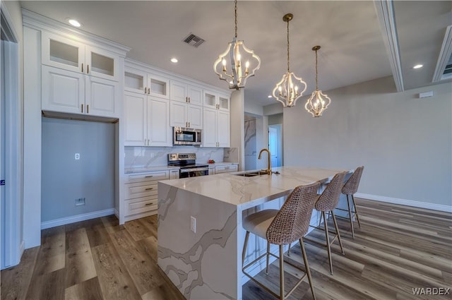 kitchen featuring appliances with stainless steel finishes, glass insert cabinets, white cabinetry, a sink, and an island with sink