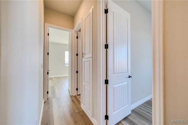 corridor featuring light wood-type flooring and baseboards