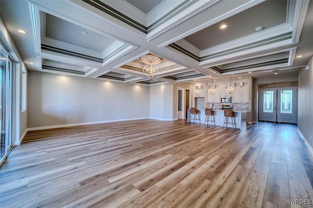 unfurnished living room with french doors, crown molding, a notable chandelier, light wood finished floors, and baseboards