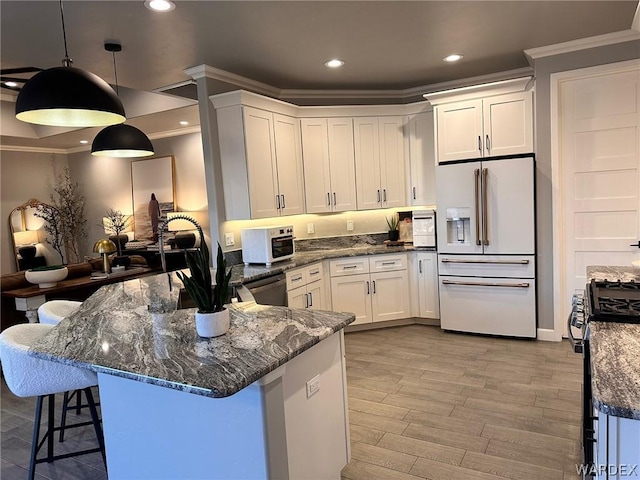 kitchen with crown molding, a breakfast bar area, hanging light fixtures, appliances with stainless steel finishes, and white cabinetry