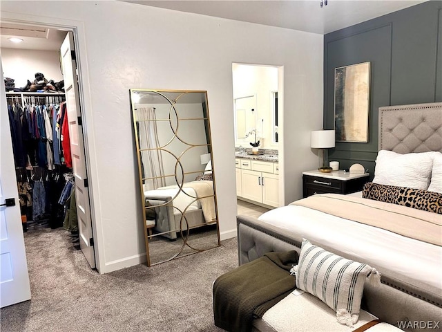 bedroom with a walk in closet, a closet, light colored carpet, ensuite bath, and baseboards