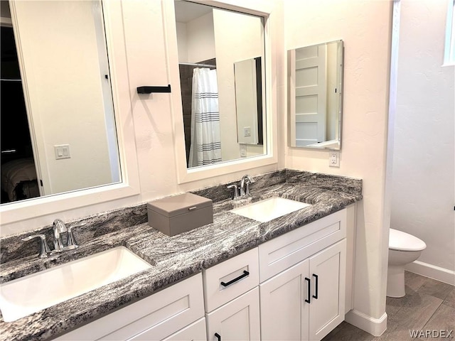 bathroom with double vanity, a sink, toilet, and baseboards