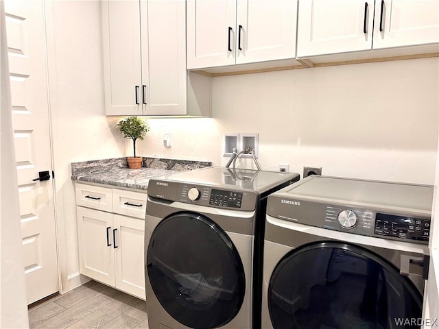 clothes washing area featuring light wood-style floors, cabinet space, and washing machine and clothes dryer