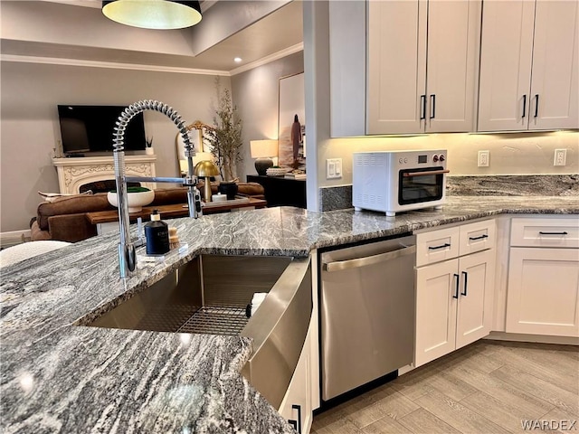 kitchen with dark stone counters, a sink, white cabinets, open floor plan, and dishwasher