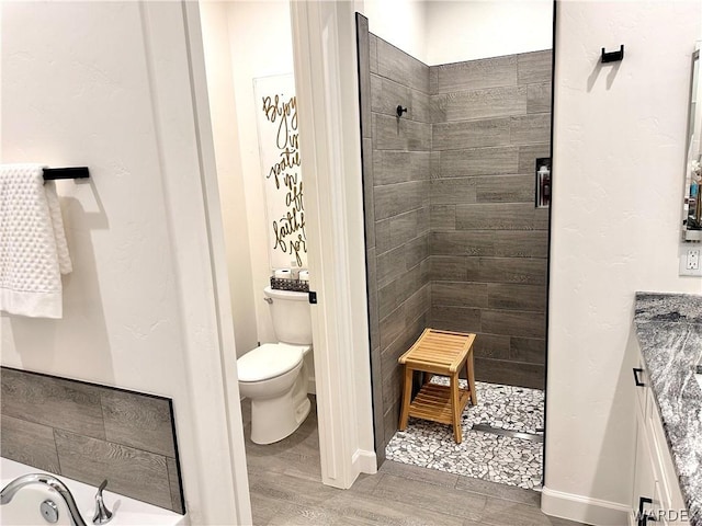 bathroom featuring toilet, wood finished floors, vanity, baseboards, and a stall shower