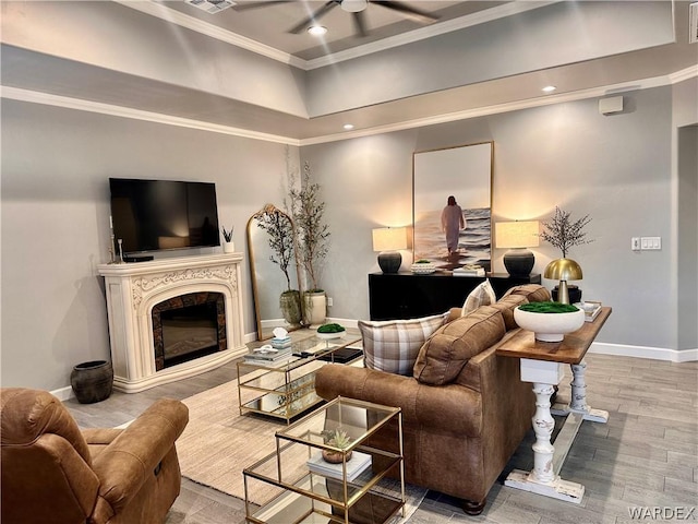 living area with ceiling fan, a premium fireplace, wood finished floors, baseboards, and ornamental molding