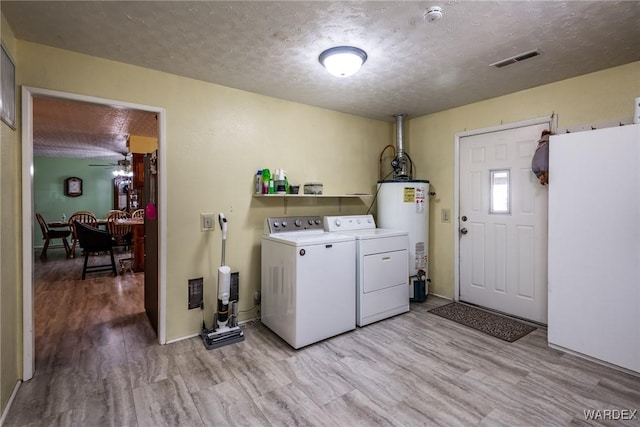 laundry area featuring washer and dryer, visible vents, water heater, and a textured ceiling