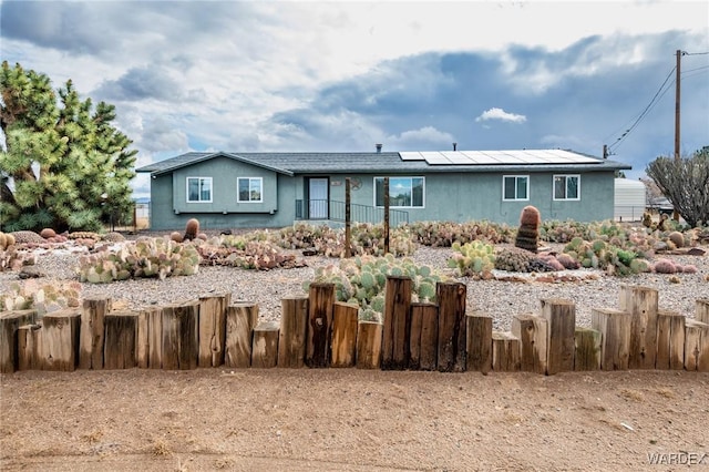 view of front facade with stucco siding, roof mounted solar panels, and fence