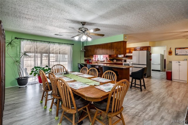 dining room featuring light wood-type flooring, a textured ceiling, visible vents, and a ceiling fan