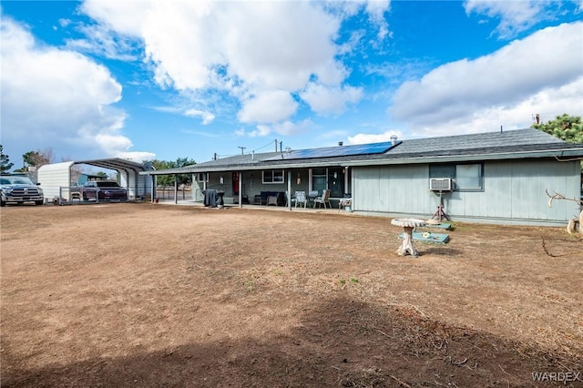 rear view of house with a detached carport, roof mounted solar panels, and a patio