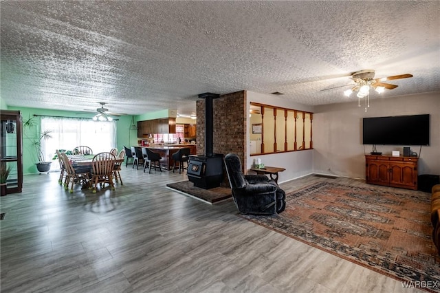 living room featuring wood finished floors, a textured ceiling, ceiling fan, and a wood stove