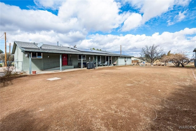 back of property with stucco siding, a patio, roof mounted solar panels, and fence