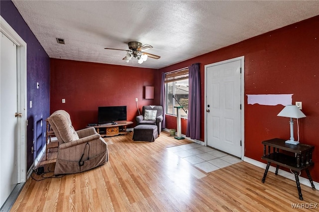 living room featuring ceiling fan, wood finished floors, visible vents, and a textured ceiling