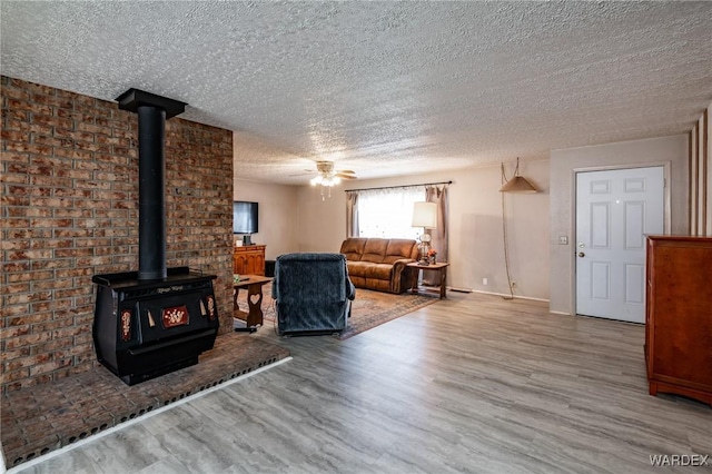 unfurnished living room featuring a textured ceiling, a wood stove, wood finished floors, and ceiling fan