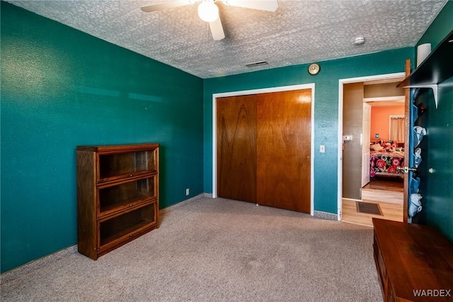 carpeted bedroom with a closet, visible vents, a textured ceiling, and ceiling fan