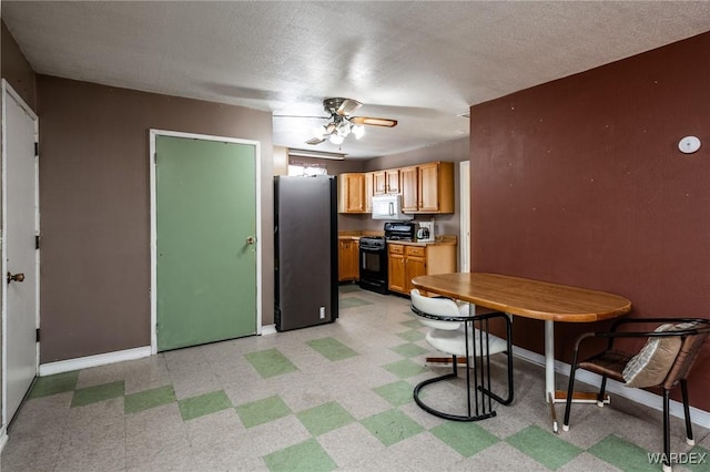 kitchen with white microwave, light floors, baseboards, black gas stove, and freestanding refrigerator