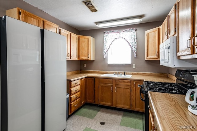 kitchen featuring white microwave, visible vents, light floors, black gas stove, and a sink