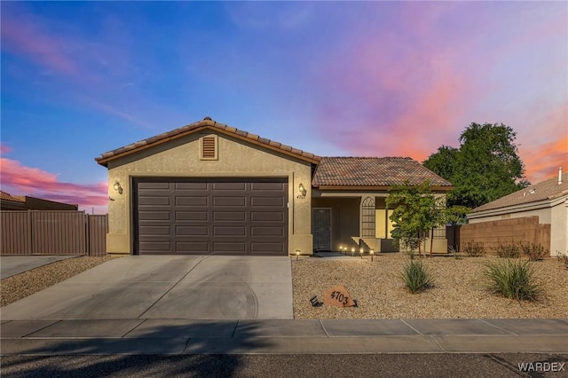 view of front facade with an attached garage, fence, concrete driveway, a tiled roof, and stucco siding