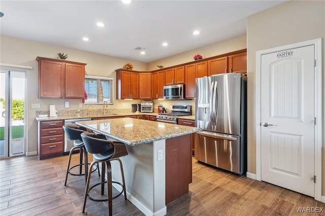 kitchen with appliances with stainless steel finishes, light wood-style floors, a kitchen island, light stone countertops, and plenty of natural light