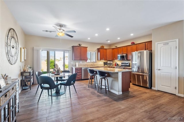 kitchen featuring light stone counters, a breakfast bar area, wood finished floors, a kitchen island, and appliances with stainless steel finishes