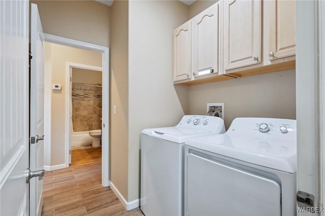 clothes washing area featuring cabinet space, baseboards, light wood finished floors, and washing machine and clothes dryer