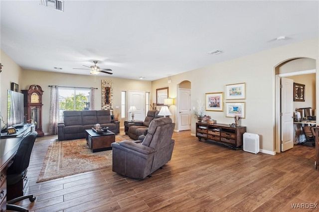 living area featuring arched walkways, visible vents, ceiling fan, and wood finished floors