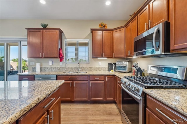 kitchen with light stone counters, stainless steel appliances, recessed lighting, a sink, and light wood-type flooring