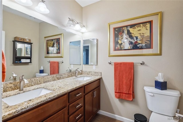 bathroom with double vanity, a sink, toilet, and baseboards