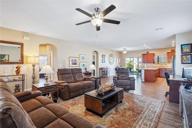 living area with baseboards, visible vents, a ceiling fan, arched walkways, and wood finished floors