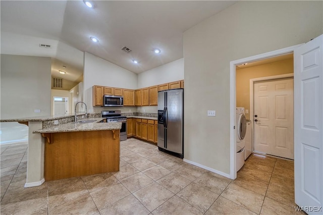 kitchen with stainless steel appliances, a peninsula, visible vents, brown cabinetry, and washer and clothes dryer