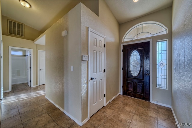 tiled foyer with lofted ceiling, a textured wall, visible vents, and baseboards