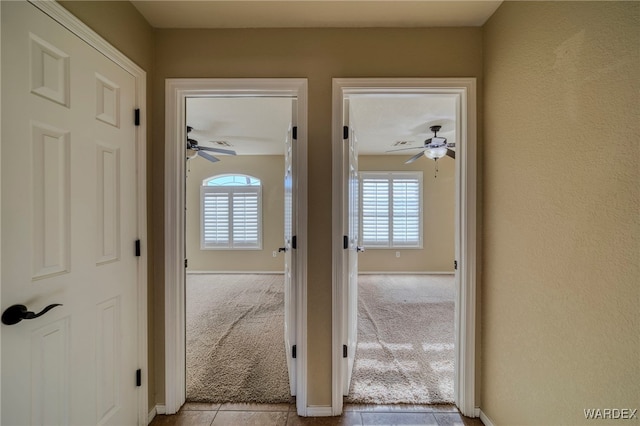 corridor featuring light carpet, baseboards, and light tile patterned flooring