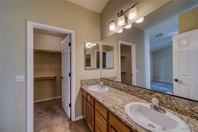 bathroom featuring visible vents, double vanity, a sink, and a walk in closet