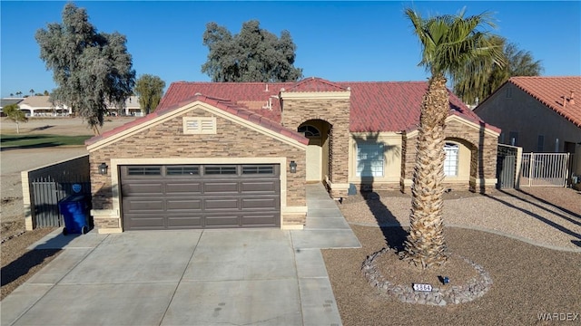 mediterranean / spanish home featuring concrete driveway, an attached garage, fence, stone siding, and a tiled roof