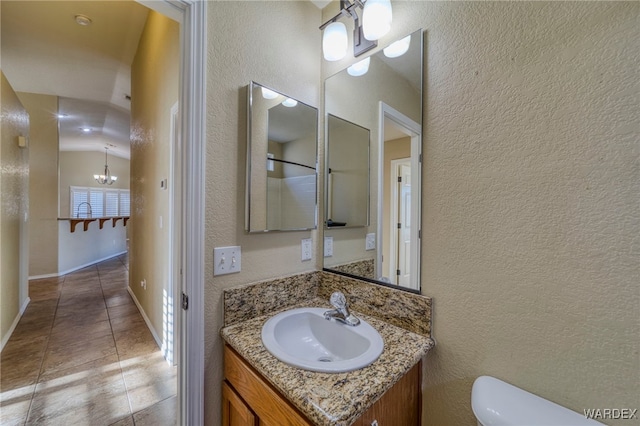 bathroom with a textured wall, toilet, vanity, tile patterned floors, and an inviting chandelier