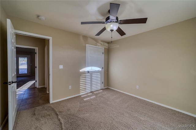 unfurnished bedroom with baseboards, dark carpet, and ceiling fan