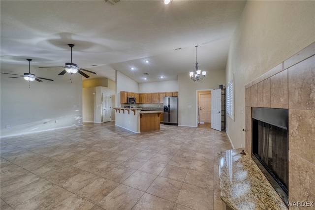 kitchen featuring a fireplace, open floor plan, appliances with stainless steel finishes, brown cabinetry, and pendant lighting