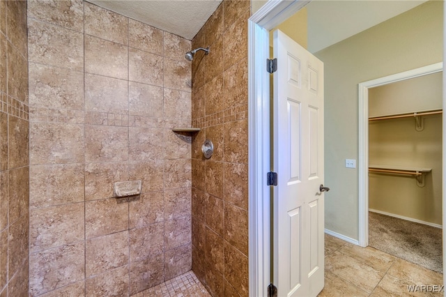 full bath featuring a spacious closet, tiled shower, and baseboards