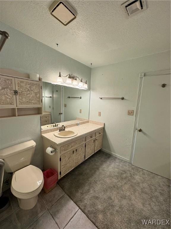 bathroom featuring a textured ceiling, a textured wall, toilet, vanity, and visible vents