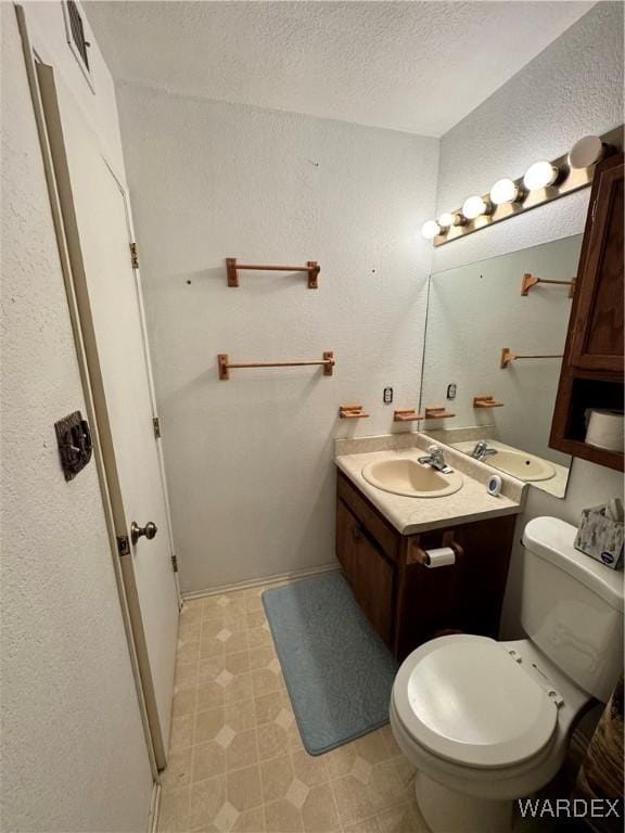 bathroom with a textured ceiling, a textured wall, toilet, vanity, and tile patterned floors