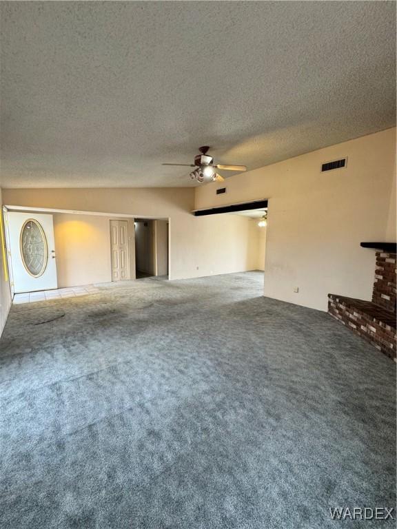 unfurnished living room featuring ceiling fan, a textured ceiling, visible vents, a brick fireplace, and carpet