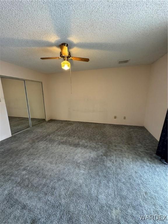 unfurnished bedroom with a textured ceiling, visible vents, a ceiling fan, a closet, and carpet