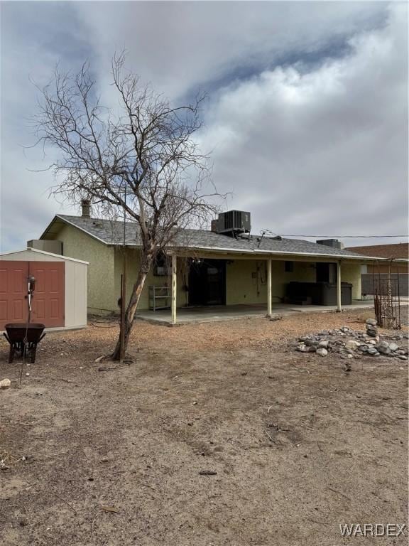 back of property with an outbuilding, stucco siding, central AC unit, a shed, and an attached carport